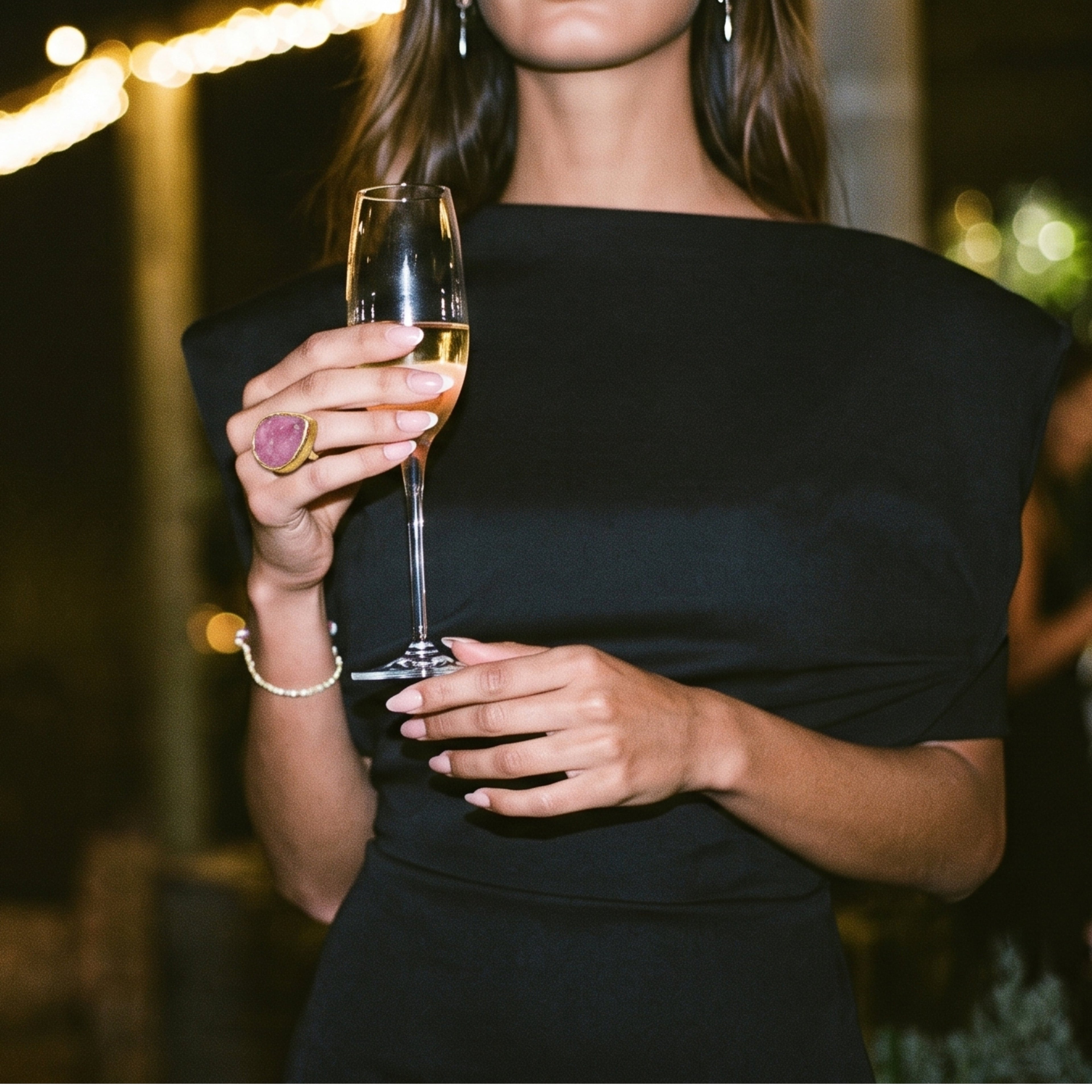 Mujer con vestido negro sosteniendo una copa en una fiesta de noche, con el anillo dorado Bahía de AMANAI con piedra rosa