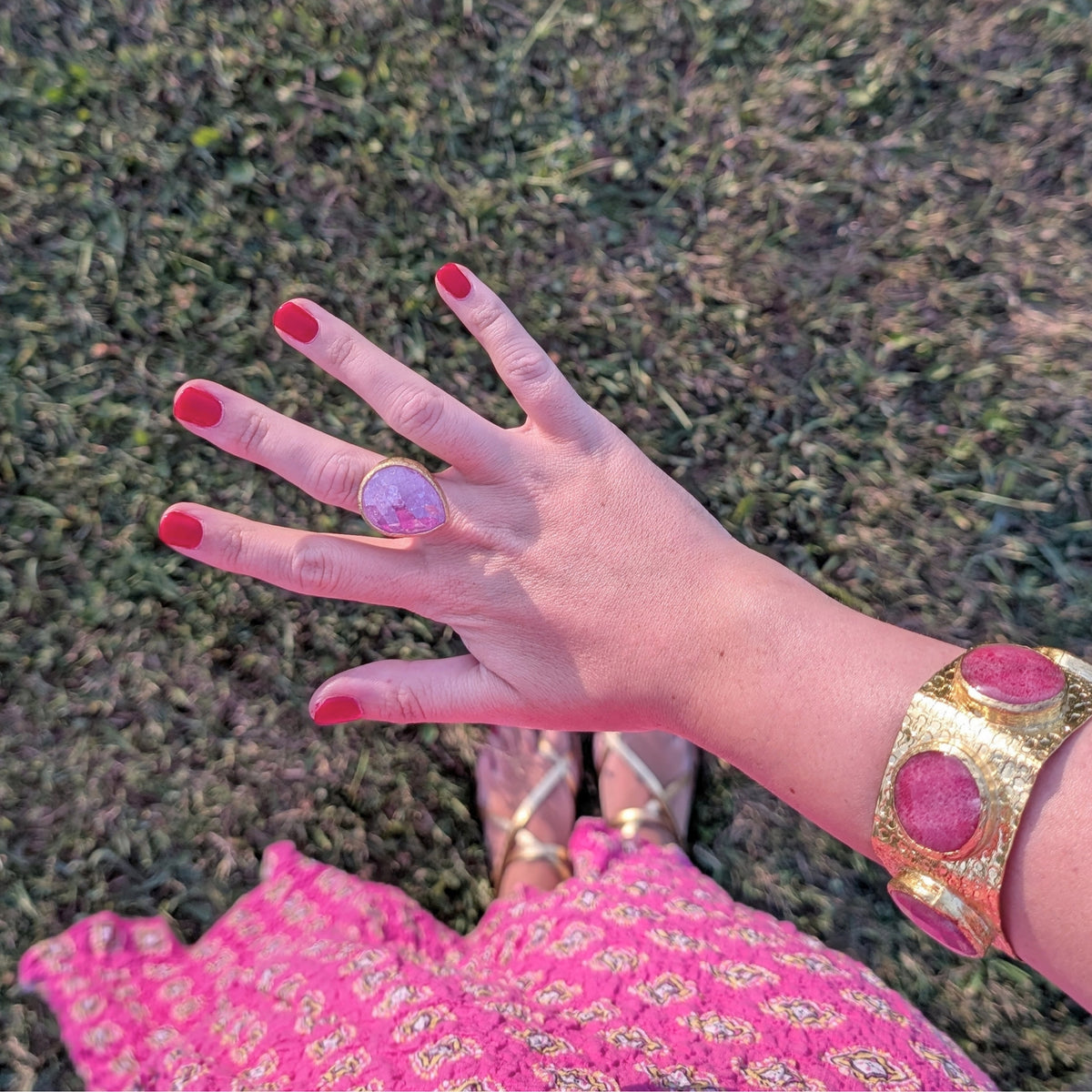 Mano con anillo dorado de piedra rosa y brazalete ancho dorado de AMANAI, joyas bañadas en oro de 18k