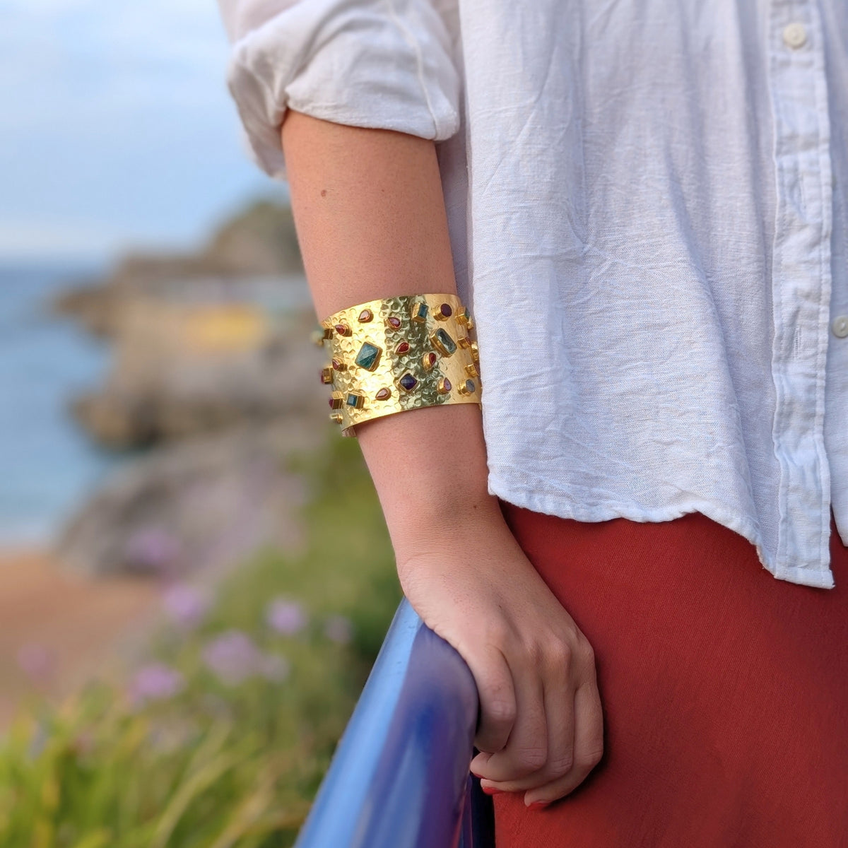 Brazalete ancho dorado martillado con piedras naturales de colores de AMANAI sobre camisa blanca y falda teja