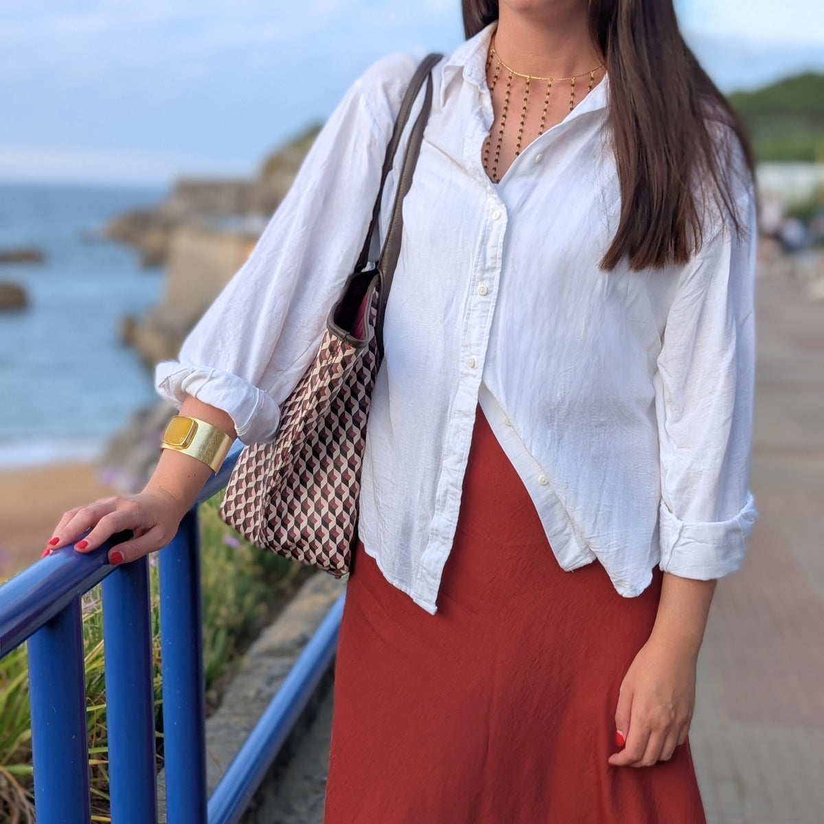 Mujer con brazalete ancho dorado con piedra amarilla y collar dorado de AMANAI en look de camisa blanca y falda teja
