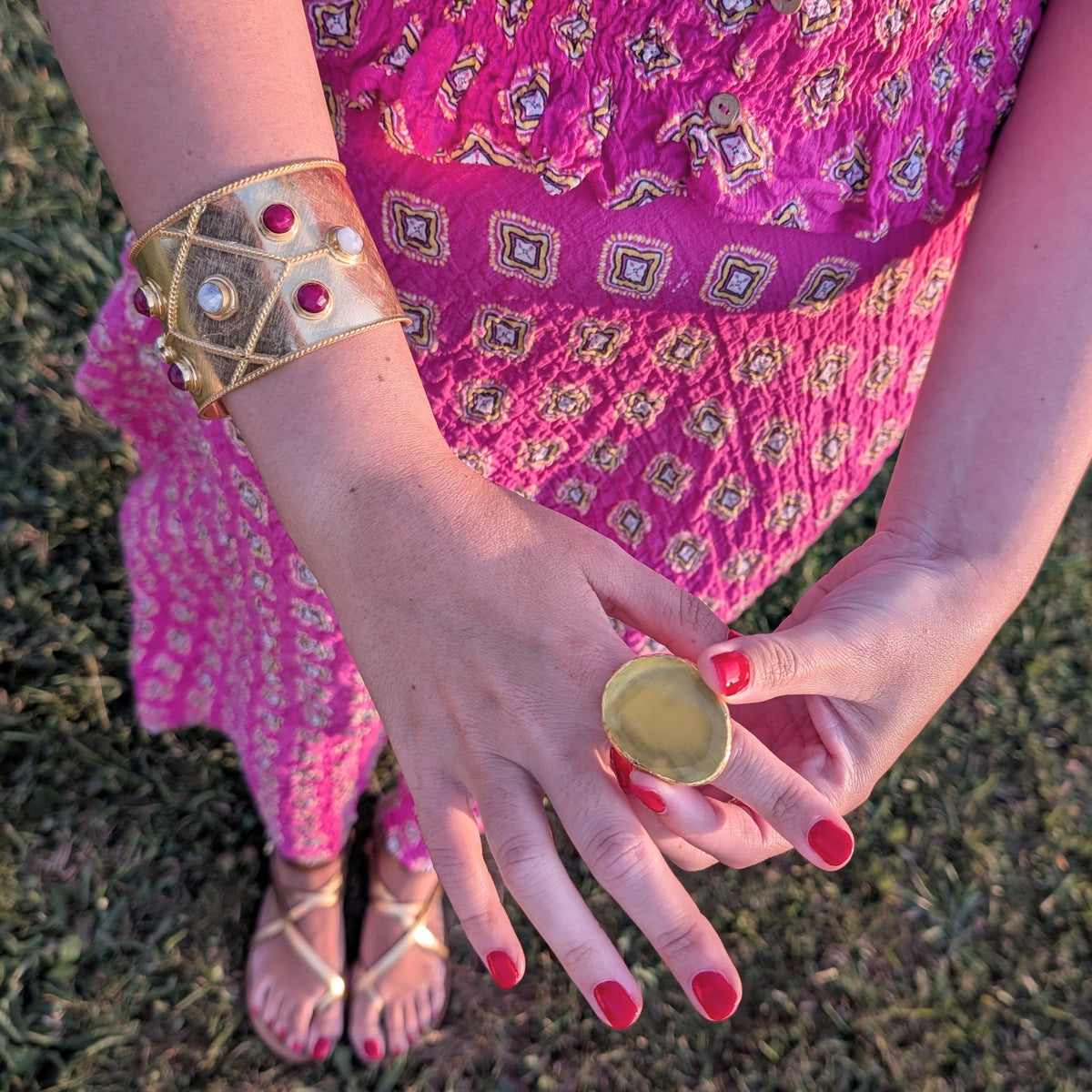 Brazalete ancho dorado con piedras naturales rojas y anillo dorado de AMANAI sobre vestido fucsia