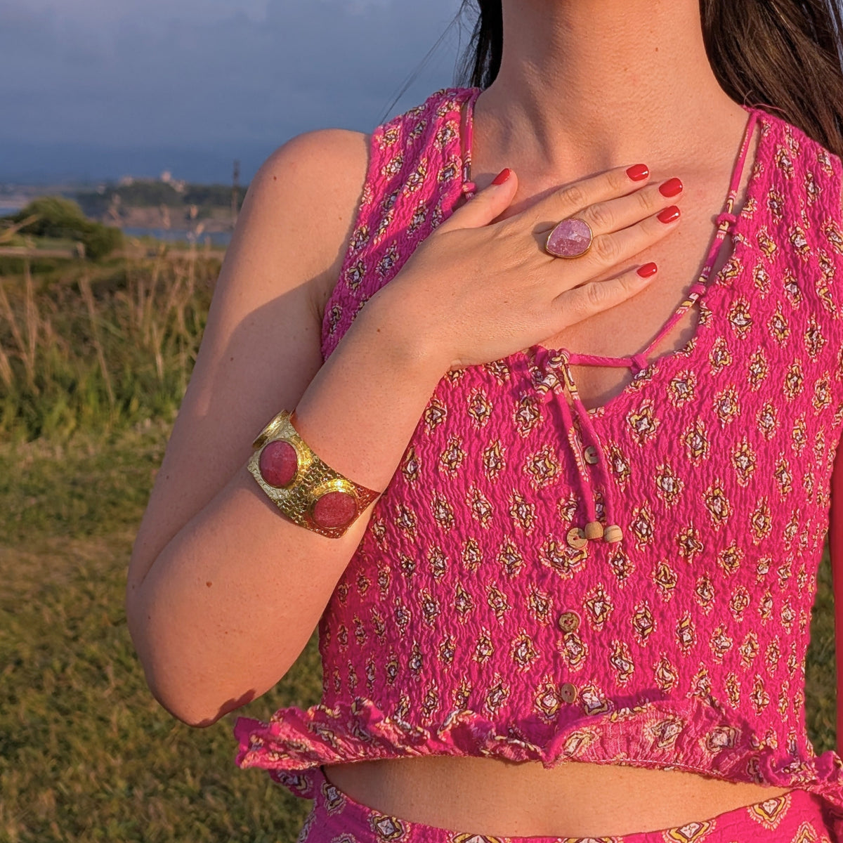 Mujer con brazalete ancho dorado con piedras naturales rosas y anillo dorado de AMANAI al atardecer
