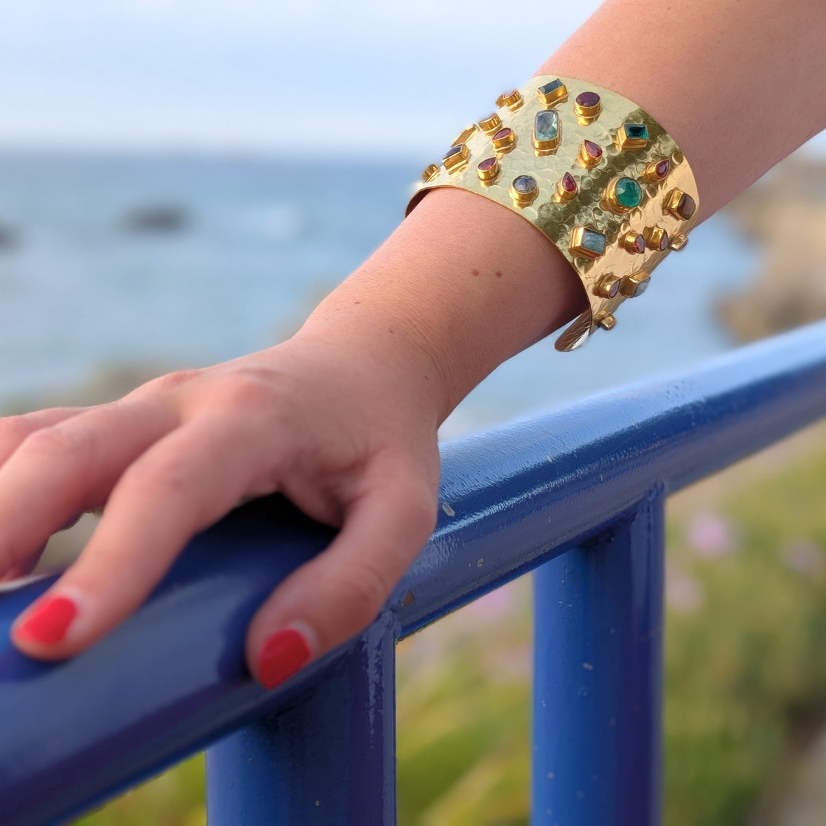 Detalle de brazalete ancho dorado de AMANAI con piedras naturales verdes, azules y granates engarzadas en oro de 18k