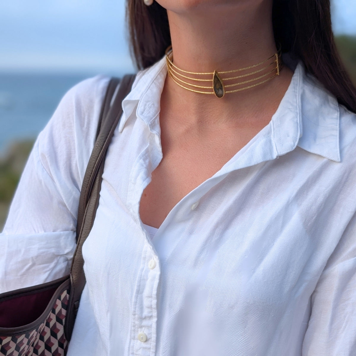 Detalle de choker dorado de cuatro aros con piedra labradorita en gota de AMANAI sobre camisa blanca