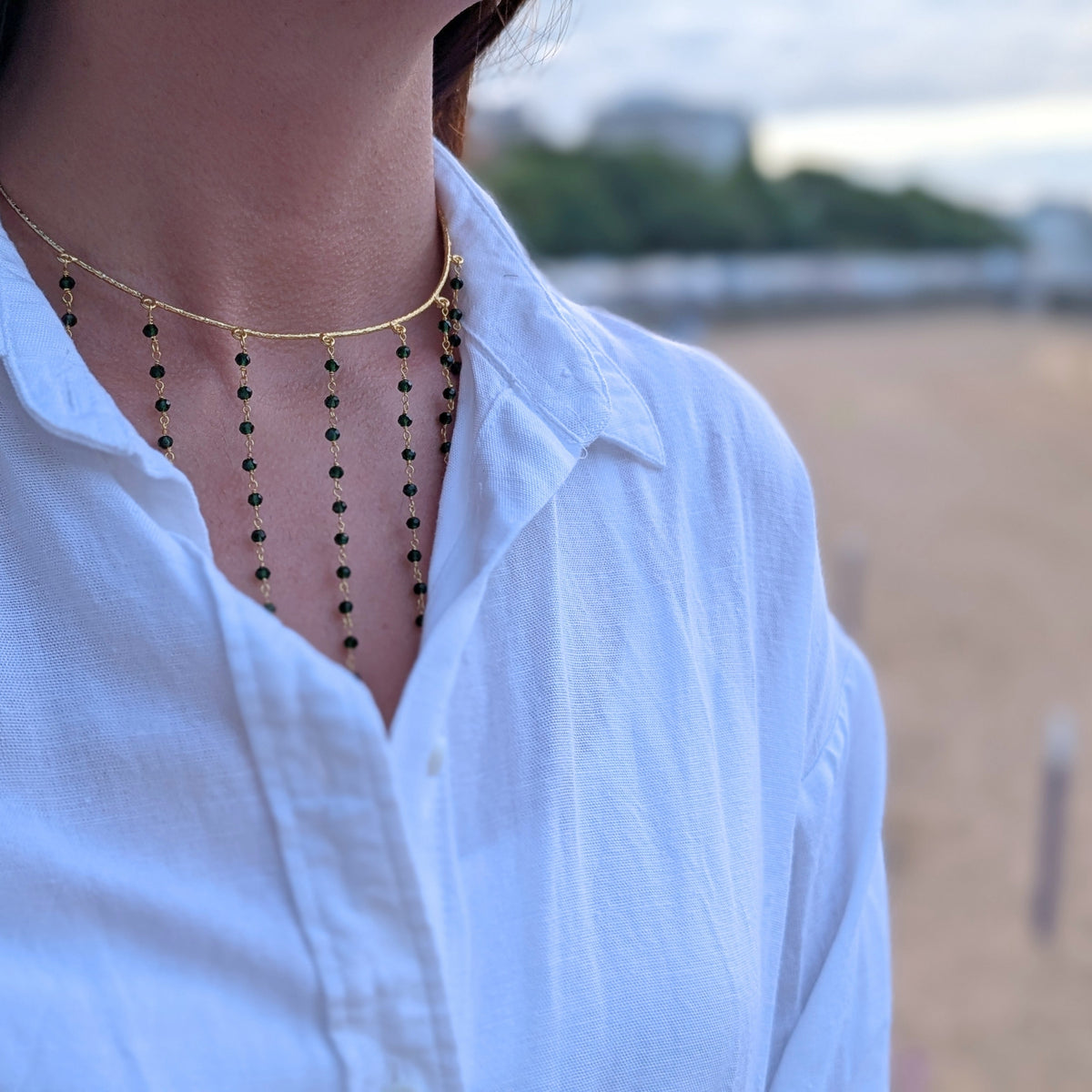 Choker dorado Isla de AMANAI con flecos de piedras verdes sobre camisa blanca de lino
