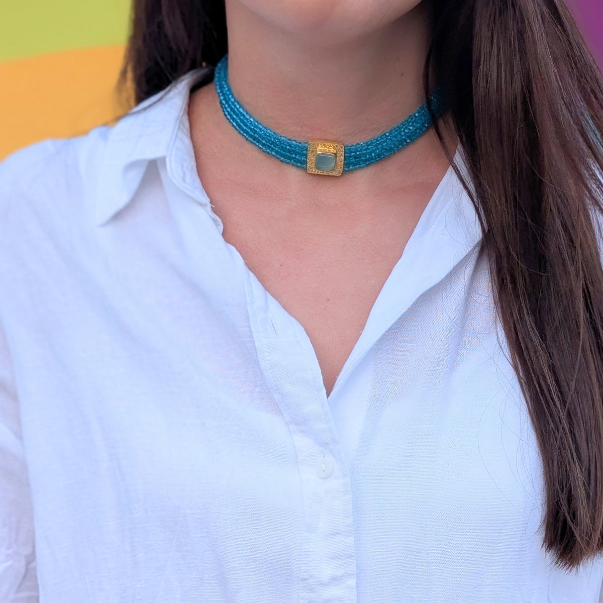 Choker de cuentas turquesa con placa dorada y piedra natural de AMANAI sobre camisa blanca