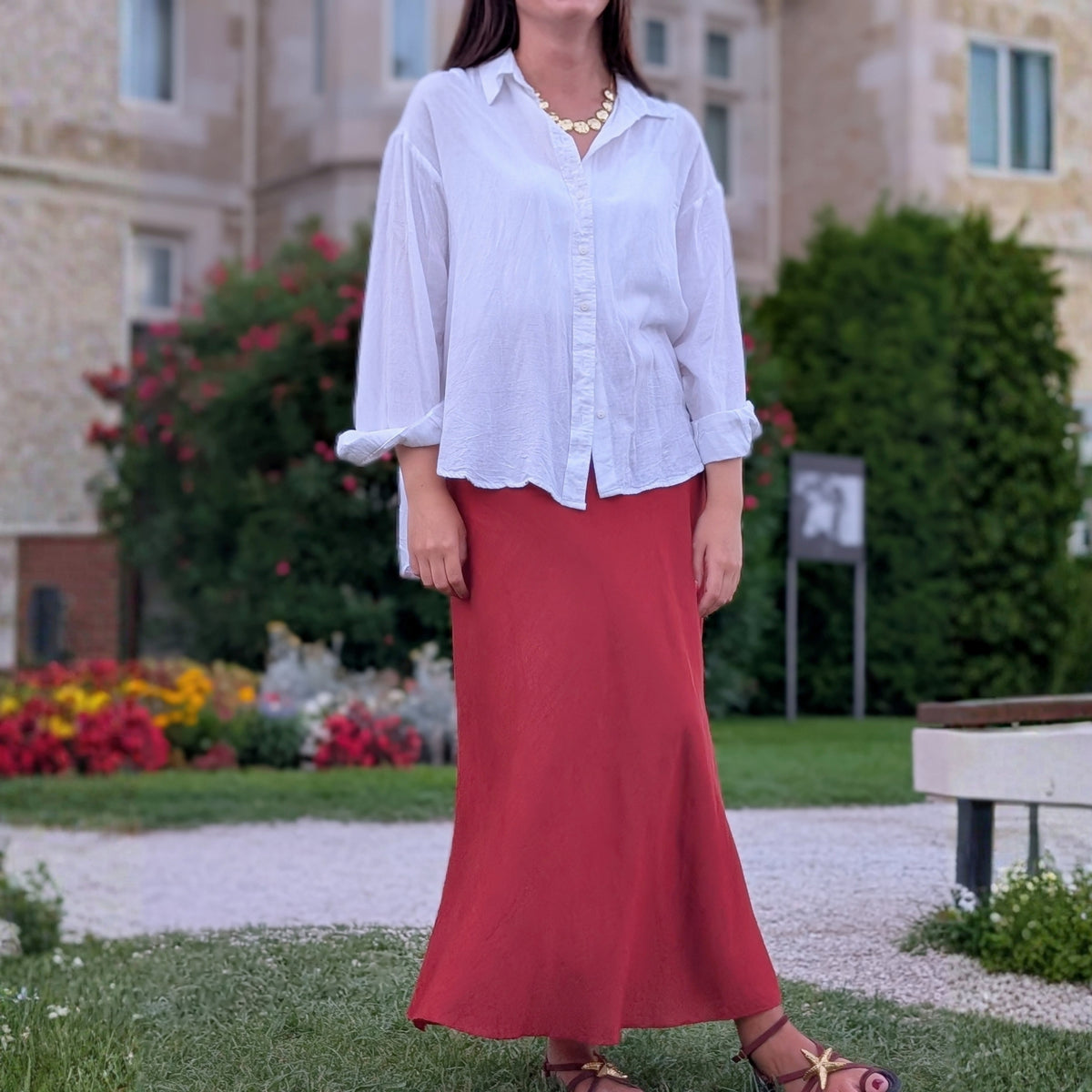 Look con collar de discos dorados martillados de AMANAI, camisa blanca y falda teja en los jardines de la Magdalena