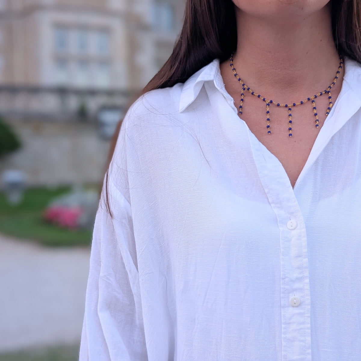Mujer con collar de cadena dorada y cuentas azules con flecos de AMANAI sobre camisa blanca