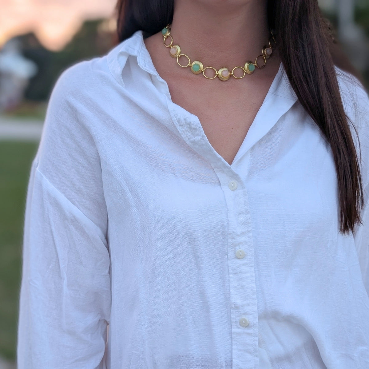 Collar Marea de AMANAI con eslabones dorados y piedras naturales verdes y rosas sobre camisa blanca al atardecer
