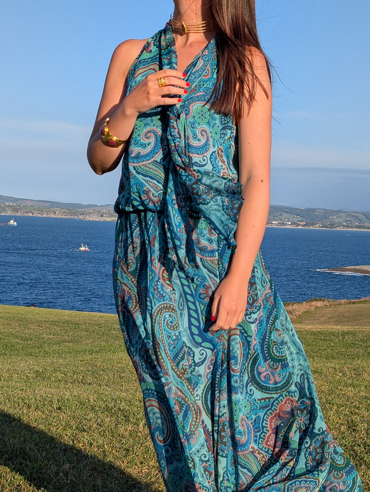 Modelo junto al mar con choker brazalete y anillo dorados bañados en oro de 18 kilates de AMANAI.