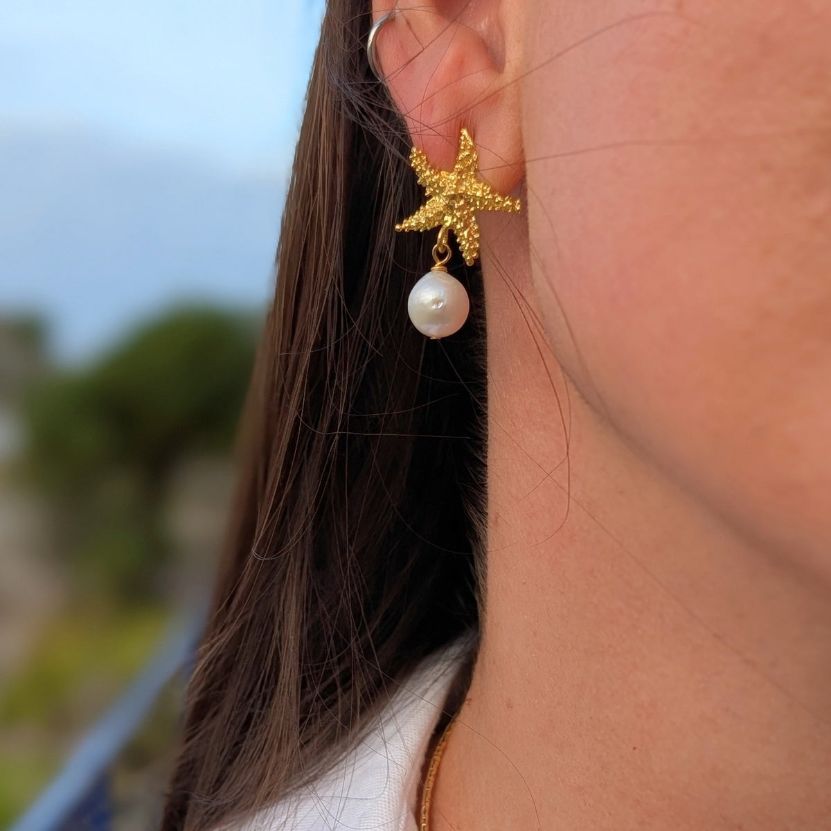 Detalle de pendiente dorado Ariel con estrella de mar texturizada y perla natural de AMANAI
