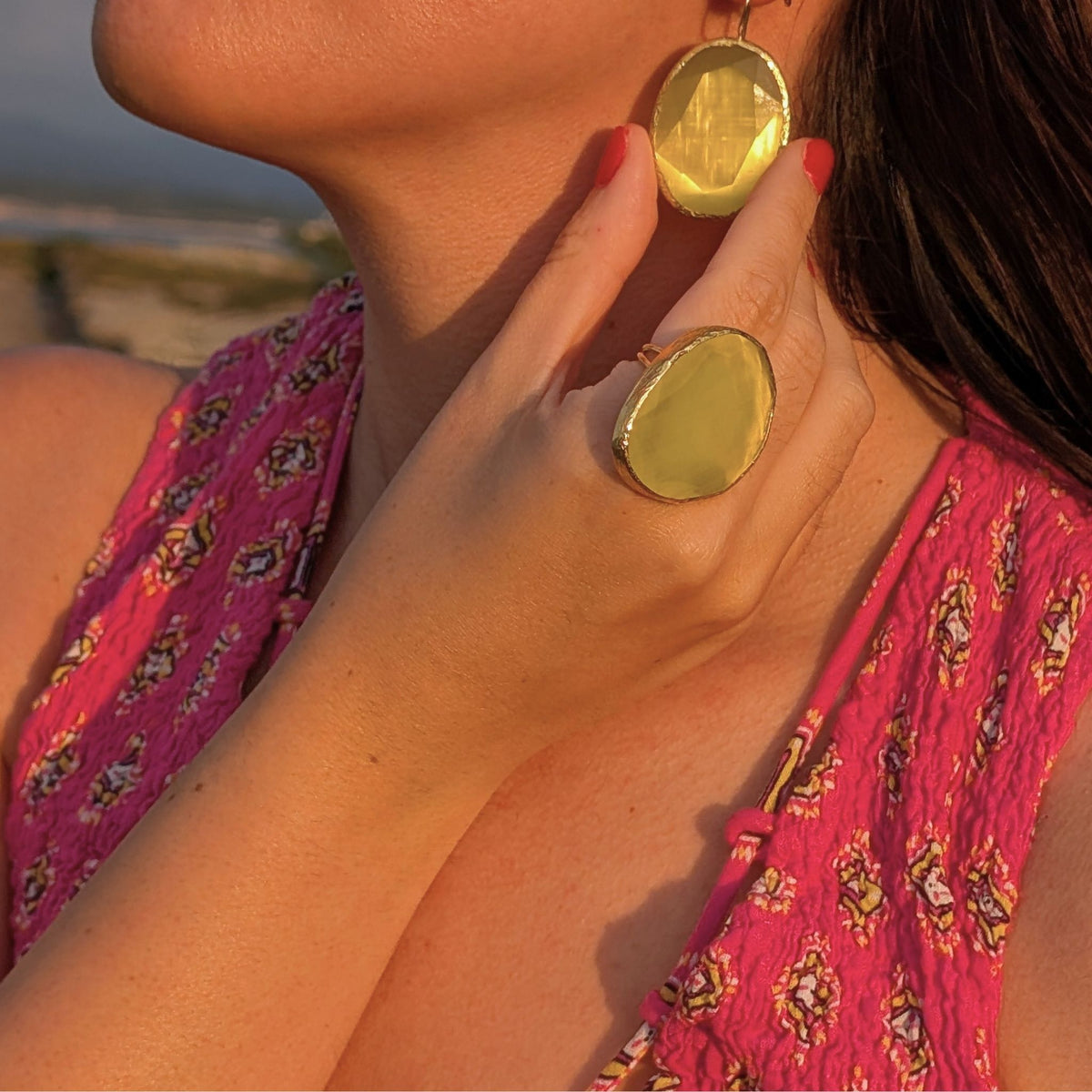 Detalle de pendientes dorados con piedra natural amarilla y anillo a juego de AMANAI al atardecer