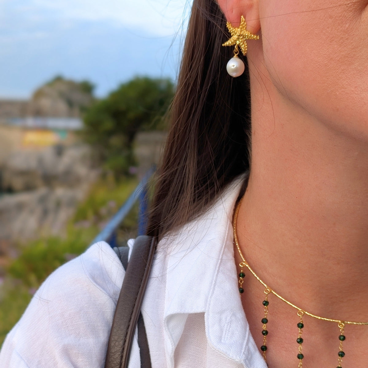Pendientes dorados Ariel de estrella de mar con perla y choker Isla de AMANAI sobre camisa blanca
